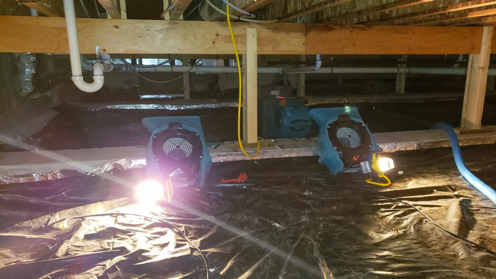 Air movers and a work light drying a crawl space covered with plastic sheeting