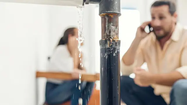 Leaking pipe dripping water while two people look on and one calls for help