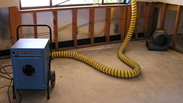 Dehumidifier and drying hose set up beside an opened wall cavity